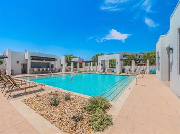 A swimming pool surrounded by a tiled patio and a small garden.